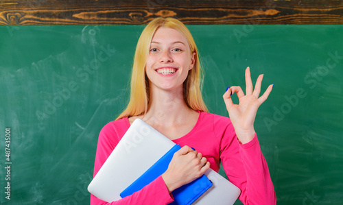 Smiling student in classroom showing okay. Female teacher with notebook make ok sign with fingers. © Svitlana