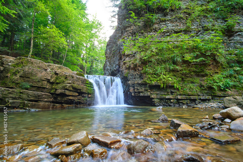 Waterfall on mountain river with white foamy water falling down from rocky formation in summer forest