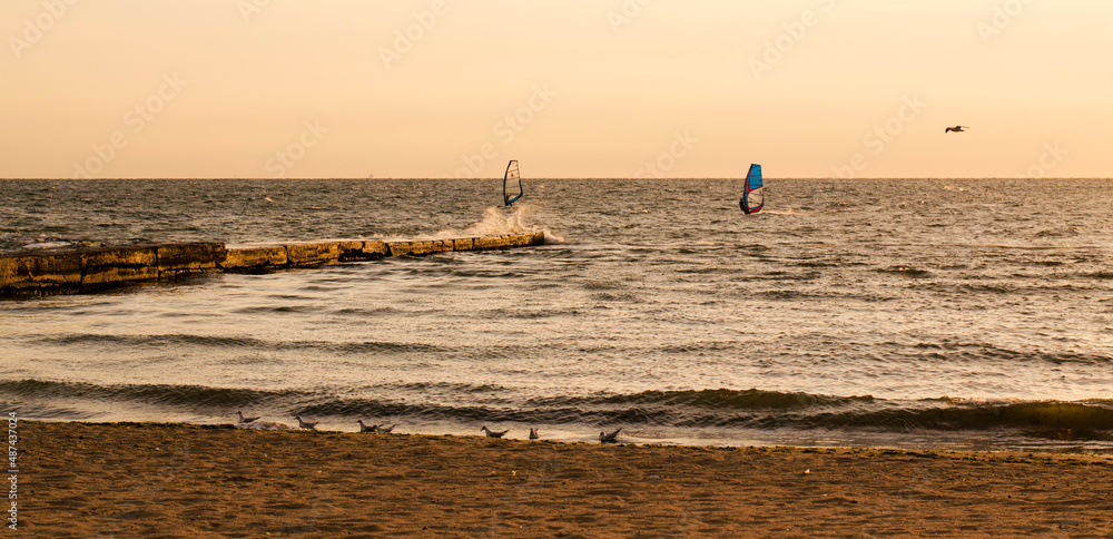 Silhouettes of windsurfers in the sea at the sunrise. People are doing sports at the dawn. Orange colours of the sunrise makes the sae look majestic.