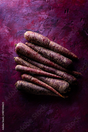 Fresh purple carrots on a rough textured purple background, with grazing light and top view