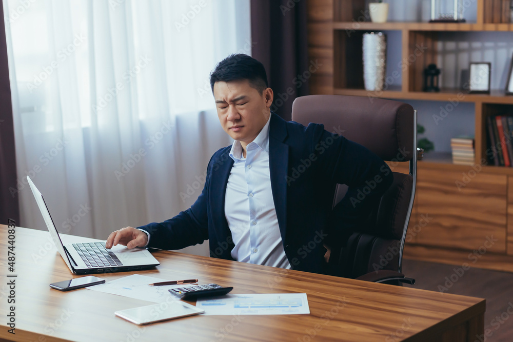 Businessman working in the office at the computer, Asian has severe back pain, boss in a classic office, reworked Businessman working in the office at the computer, Asian has severe back pain, boss in a classic office, reworked
