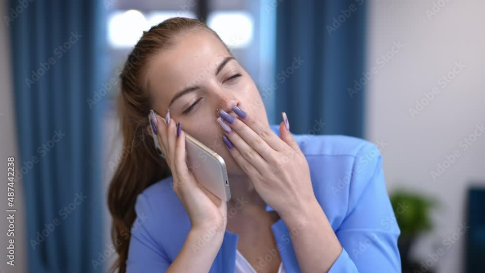 Young bored businesswoman yawning talking on phone indoors. Front view portrait of disinterested Caucasian beautiful woman in elegant blue suit. Restlessness and boredom concept Young bored businesswoman yawning talking on phone indoors. Front view portrait of disinterested Caucasian beautiful woman in elegant blue suit. Restlessness and boredom concept