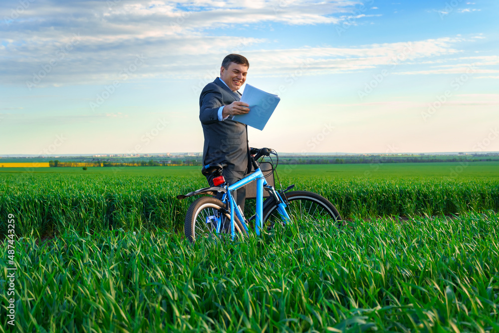 businessman dressed in a business suit, poses with bicycle in green grass field and reads documents, beautiful nature in spring, business concept businessman dressed in a business suit, poses with bicycle in green grass field and reads documents, beautiful nature in spring, business concept