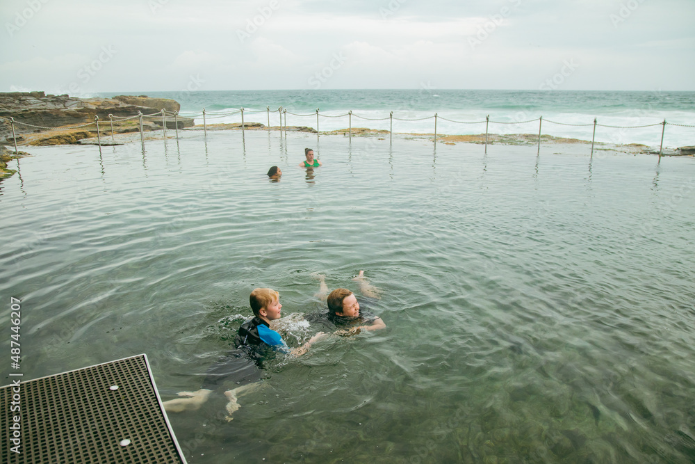 Fototapeta premium Brothers swimming at the Bogey Hole in Newcastle, NSW on an overcast day with rough surf