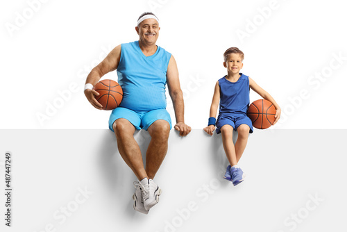 Mature man in jersey holding a basketball and sitting on a blank panel with a little boy