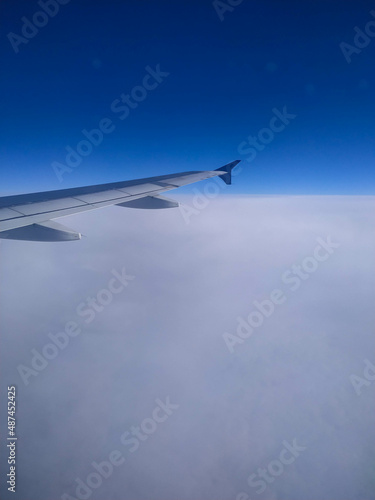The view from the plane window on a cloudy sky in winter. Cabin window, snow, blue sky, plane wing, frozen plane window, flying. View on earth from a plane.