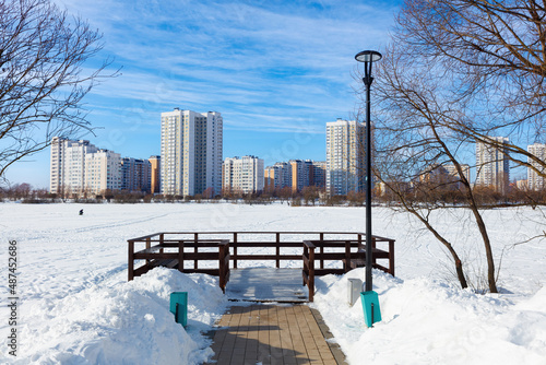 Winter ice fishing, lake, frosty day. A fisherman is engaged in ice fishing in the pond of the city park. Against the background of a multi-storey, modern, residential development.