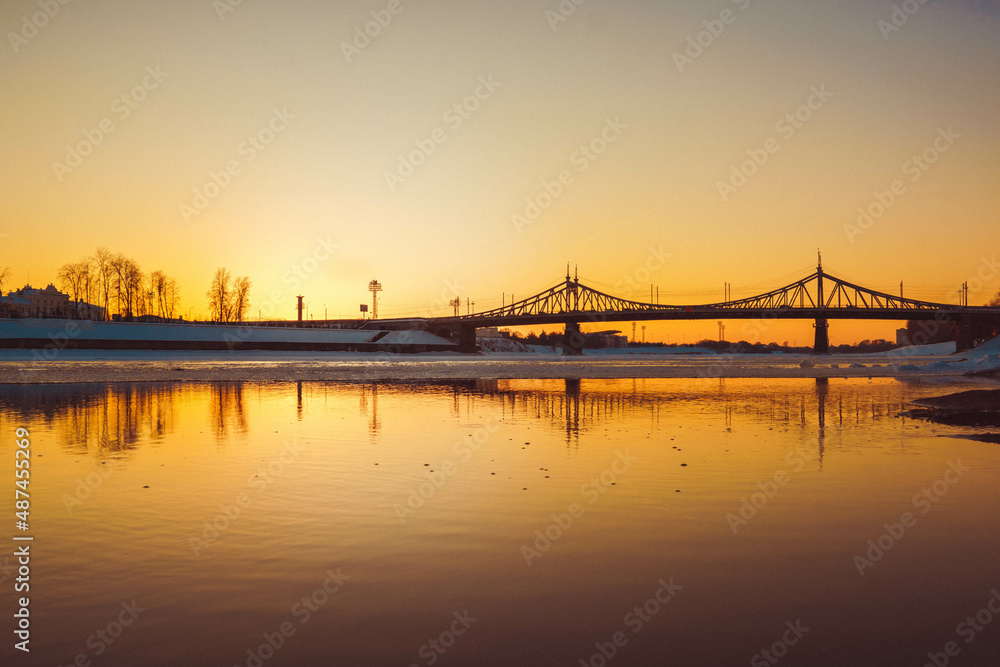 a bridge across the river, trees and houses in the background, photos at sunset