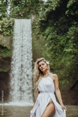 a young beautiful girl at a waterfall in a white wedding dress, a girl in the tropics against the backdrop of a waterfall, young beautiful blonde in a white dress