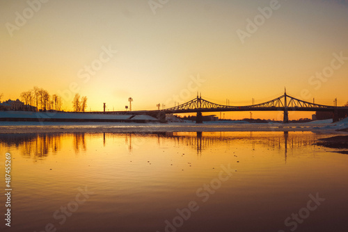 a bridge across the river, trees and houses in the background, photos at sunset