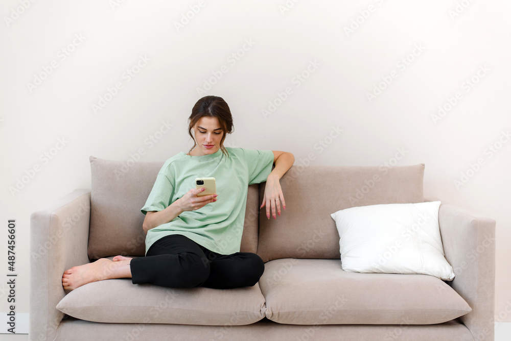 Image of happy optimistic young woman sitting indoors at home and shopping or social media using mobile phone on sofa at home.