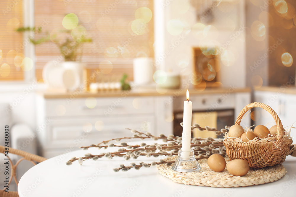 Basket with Easter eggs, pussy willow branches and burning candle on dining table Basket with Easter eggs, pussy willow branches and burning candle on dining table