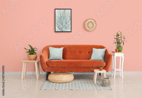 Stylish orange sofa with houseplants in modern interior of living room