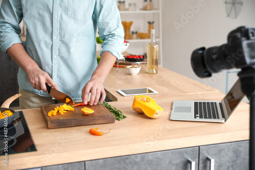 Young man cutting squash while recording video tutorial in kitchen