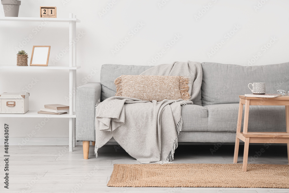 Comfortable sofa, shelf unit, stepladder stool and wicker carpet in living room interior