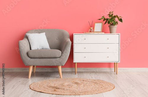 Comfortable armchair, chest of drawers and wicker carpet in room interior photo