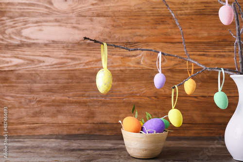 Different Easter eggs and vase with tree branches on wooden background
