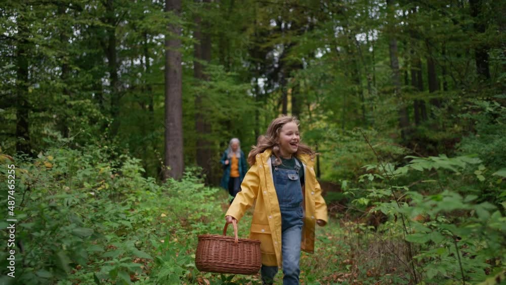Happy little girl with basket running during walk with mother and grandmother outdoors in forest Happy little girl with basket running during walk with mother and grandmother outdoors in forest