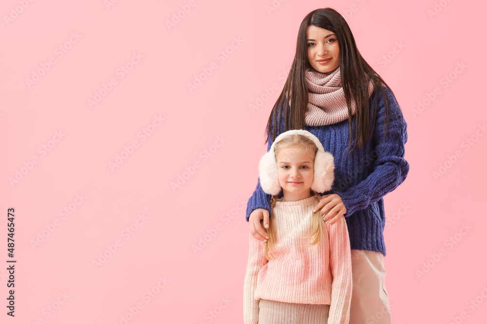 Little girl and her mother in warm sweaters on pink background