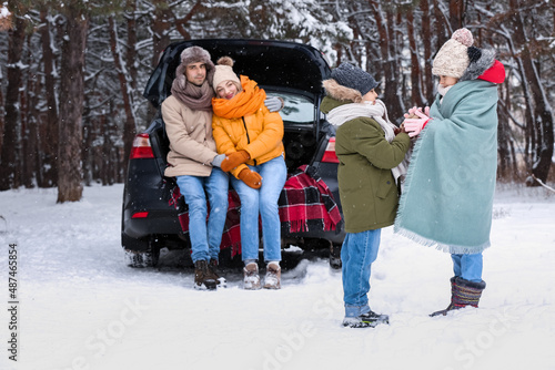 Happy children with their parents and car in forest on snowy winter day