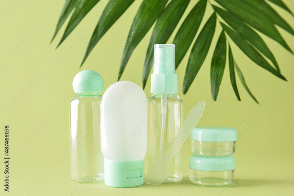 Set of travel bottles, jars and palm leaf on green background Set of travel bottles, jars and palm leaf on green background