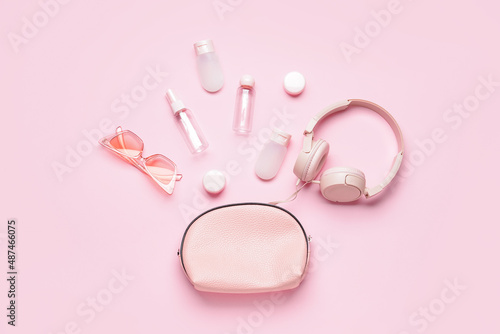 Composition with cosmetic bag, empty travel bottles, sunglasses and headphones on pink background