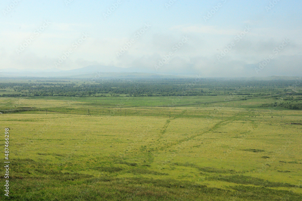 Fototapeta premium Endless steppe and a large forest at the foot of a mountain range with peaks in the clouds.