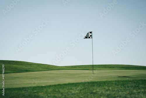 Golf flagstick waving in a green field with a light blue sky in the background