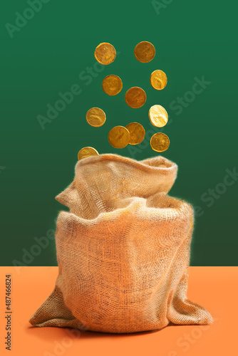 Golden treasure minimal concept. Bag full of golden coins with many coins lifted out of it.Pastel green and terracotta background.