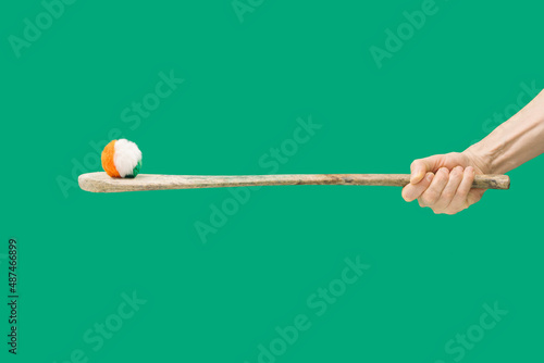 Ireland traditional sport minimal concept. Man hands hold hurly sticks – hurleys. Fluffy ball with Irish colors on top of it against an green background