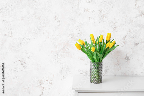 Vase with beautiful tulips on chest of drawers near grunge wall