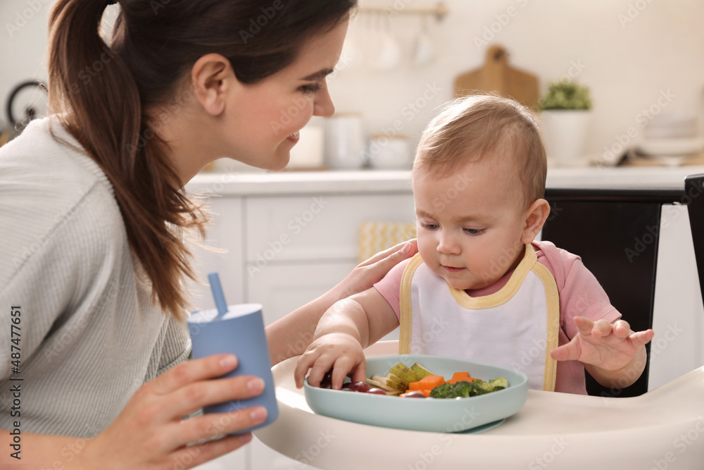 Mother feeding her cute little baby in kitchen