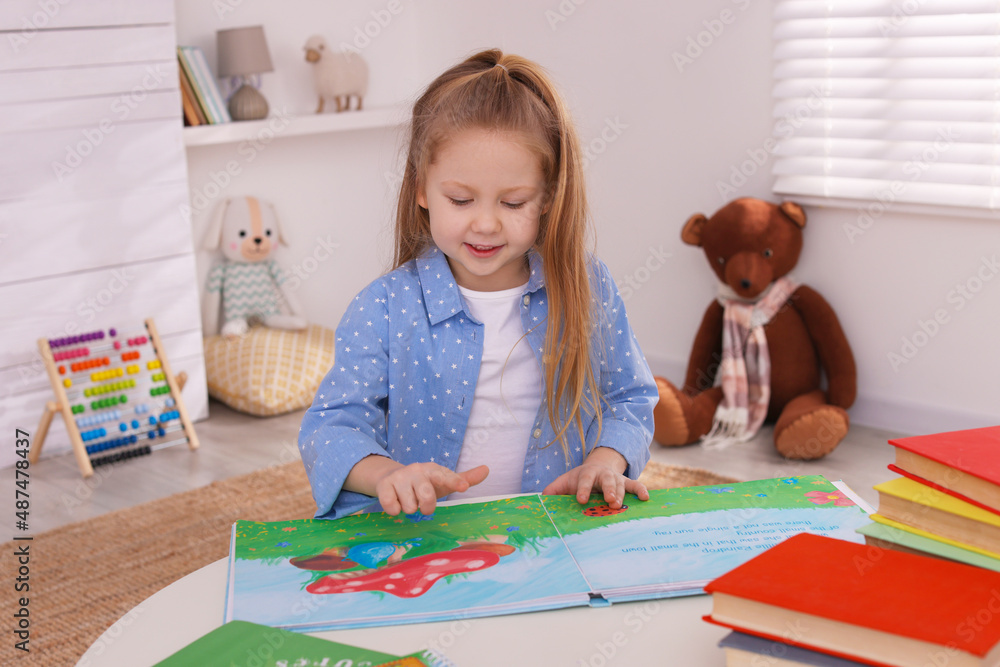 Cute little girl reading book at table in room Cute little girl reading book at table in room