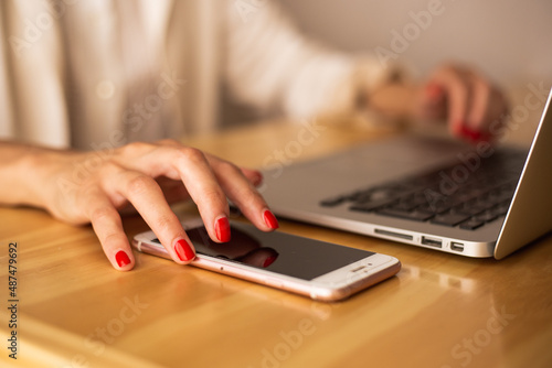 woman's hand touching a cell phone on a table with a laptop