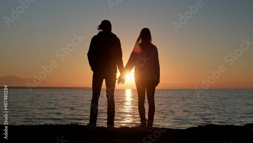 Silhouette of loving couple holding hands against sunset.