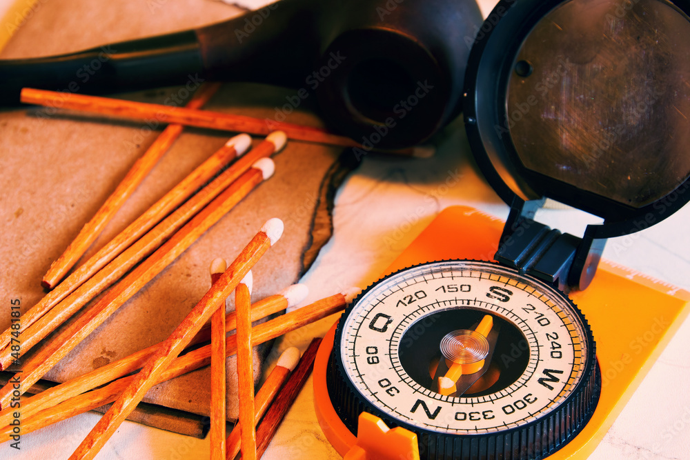 Fototapeta premium Adventurer compass, smoking pipe and matches on the burned papers. Explorer cabinet backgrounds and treasures hunting