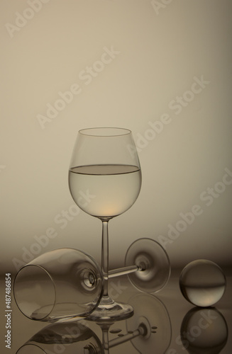 Still-life. Two large glasses of thin glass for wine and a ball of glass on a light background