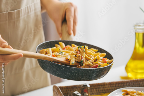 Φωτογραφία Woman with frying pan of cajun chicken pasta on table in kitchen