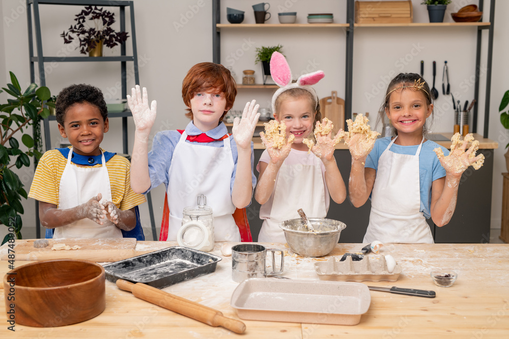 Adorable little sisters looking at camera with wide smiles while standing at wooden table and preparing healthy snack for their parents Adorable little sisters looking at camera with wide smiles while standing at wooden table and preparing healthy snack for their parents