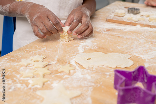Kids in white aprons cutting figures in rolled dough while making tasty cookies for holiday