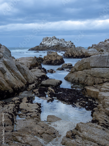 A rocky section of coastline near Monterey Bay in California, on an overcast day at sunset, long exposure.