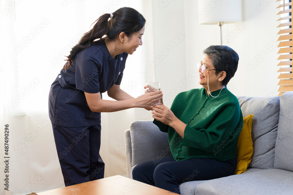 Obraz premium Smiling nurse giving glass of water to senior asian woman in nursing home or assisted living facility.