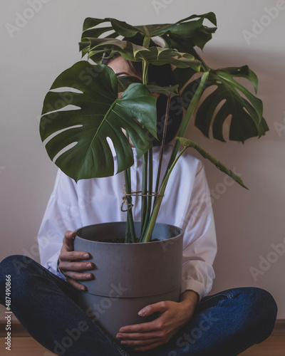 Young woman is sitting with a big flower pot with monstera