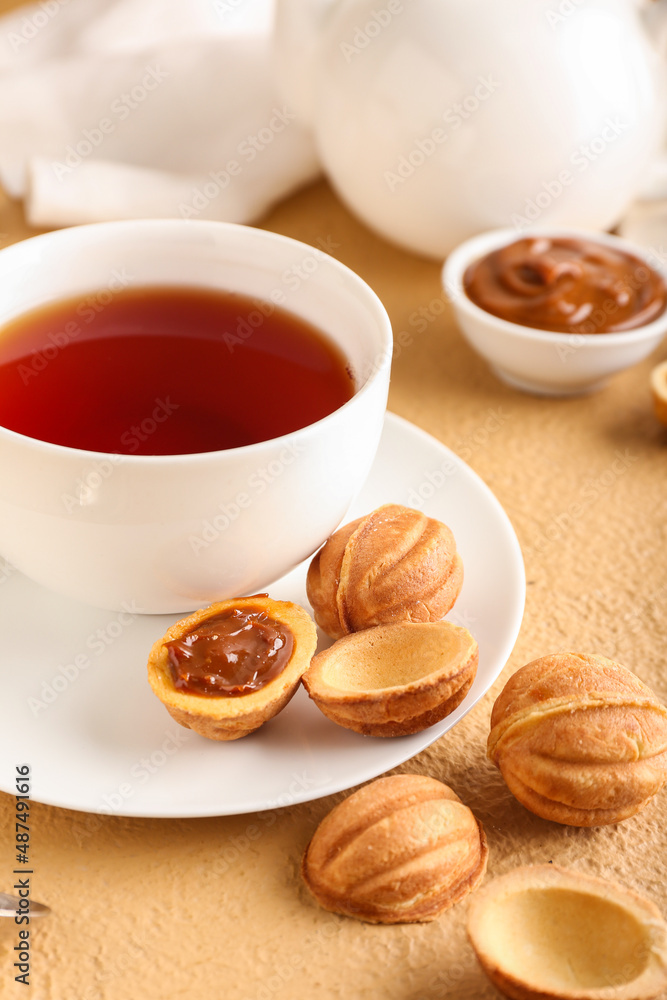 Tasty walnut shaped cookies with boiled condensed milk and cup of tea on beige background