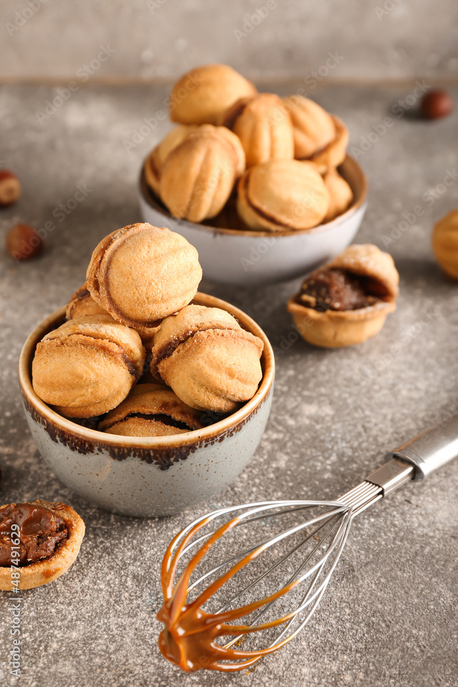 Bowls of tasty walnut shaped cookies with boiled condensed milk on grey background