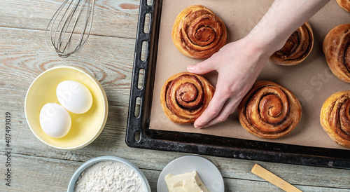 Woman hands are carefully taking out fresh warm cinnamon rolls buns from a baking tray. Concept of delicious homemade pastry and cozy atmosphere