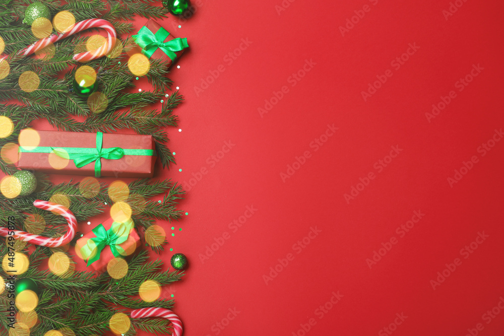 Flat lay composition with fir tree branches, Christmas decor and gift boxes on red background, space for text. Bokeh effect