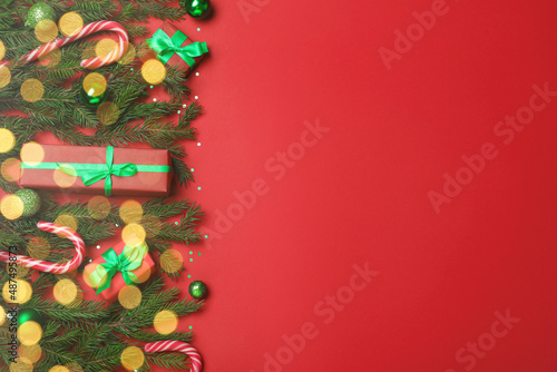 Flat lay composition with fir tree branches  Christmas decor and gift boxes on red background  space for text. Bokeh effect