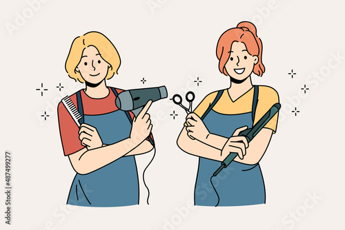 Working as hairdresser in salon concept. Two young smiling girls wearing aprons standing holding working tools in hairdressing salon vector illustration 