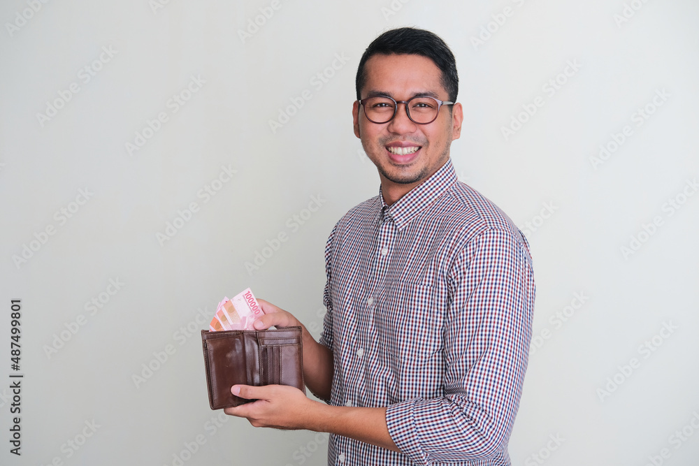 Adult Asian man smiling to the camera while taking paper money from his wallet Adult Asian man smiling to the camera while taking paper money from his wallet